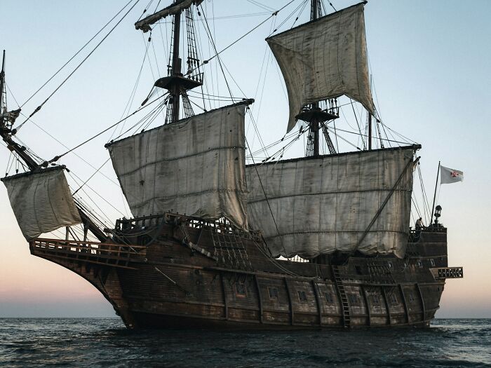 A large, historic wooden sailing ship with unfurled sails on the water. Uncover amazing history facts.