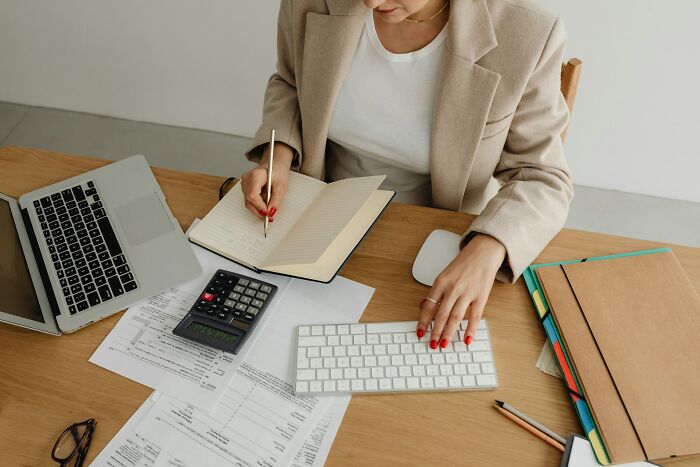 A woman working at a desk with a laptop, calculator, and papers. Hilarious micro feminism clap backs.