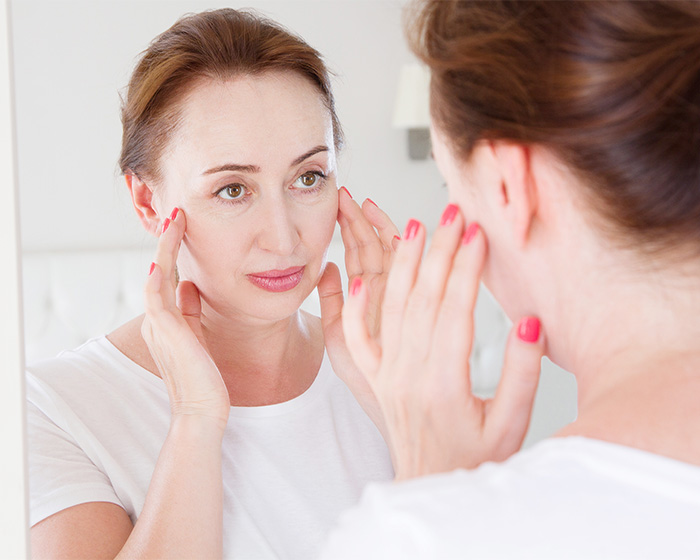 Woman looking in a mirror, checking her skin, possibly concerned about health and libido.