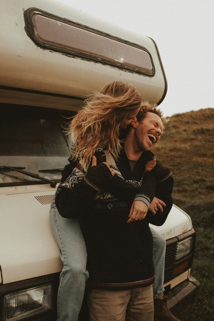 A couple embracing and laughing on the front of a camper van, illustrating happiness before getting married.