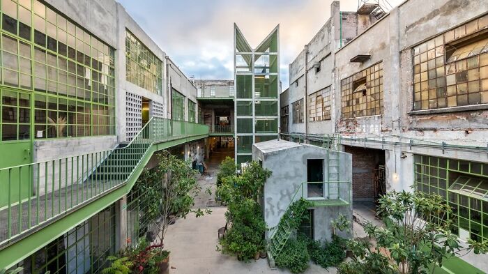An exterior view of an architectural complex with green metal walkways and lush plants, showcasing remarkable designs.