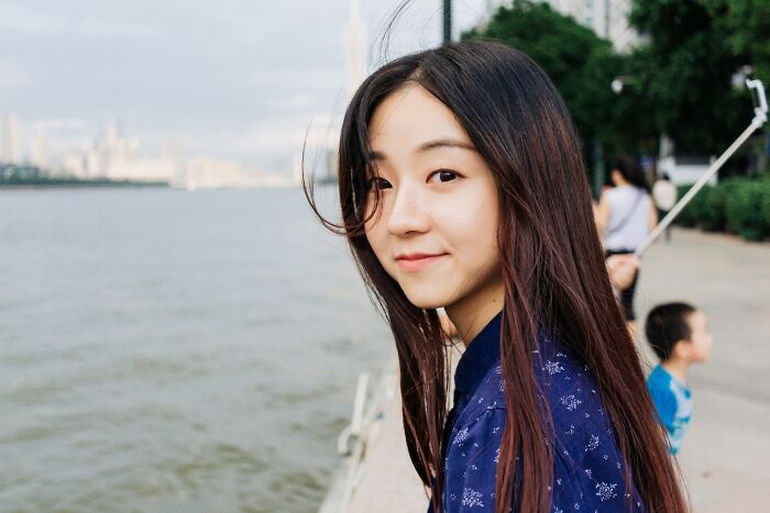 A young woman smiles by a river, representing international partners experiencing various culture shocks.