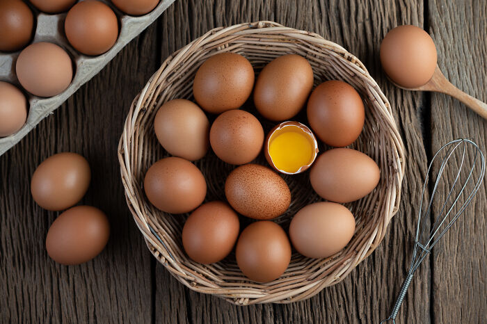 Farm-fresh brown eggs in a woven basket and carton, with one cracked egg showing a vibrant yolk. Perfect for World War II veterans' recipes.