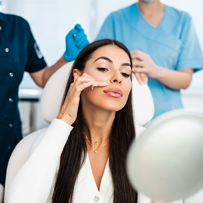 Woman in a cosmetic procedure setting, looking at her reflection, contemplating the dramatic face changes. Woman in a cosmetic procedure setting, looking at her reflection, contemplating the dramatic face changes.