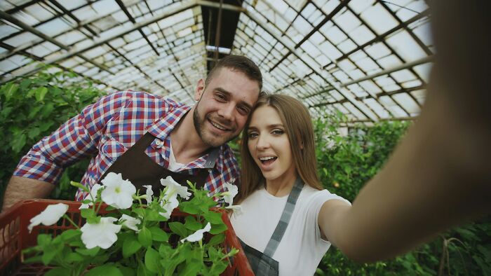 A happy married couple taking a selfie in a greenhouse with plants, showing the realities of being married.