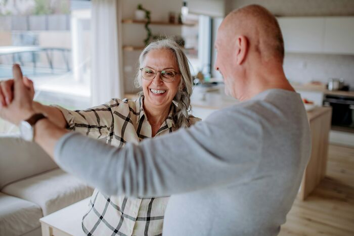 An elderly couple joyfully dancing in their living room, representing the beautiful realities of being married.