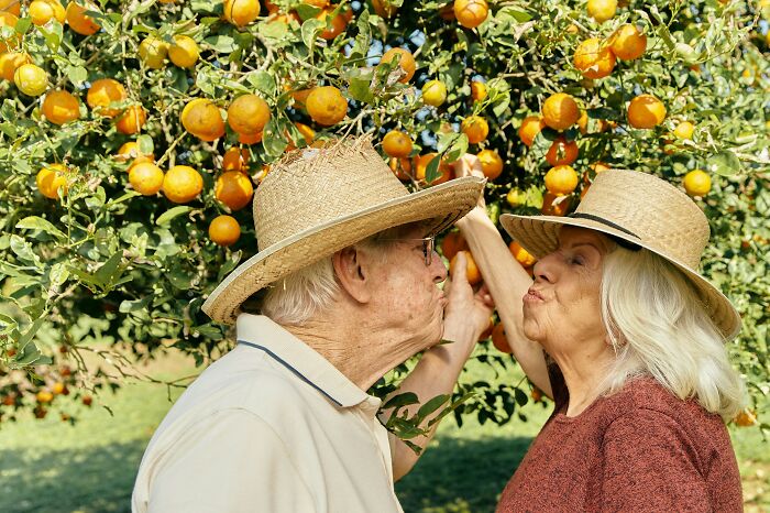 An older couple making a kissy face under a fruit tree, illustrating the realities of being married.