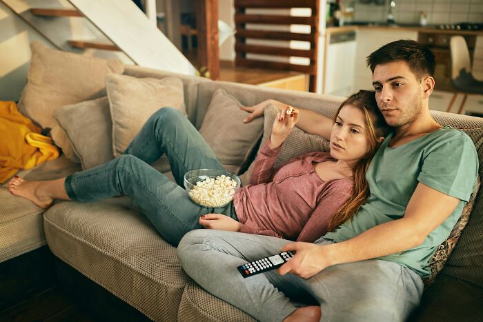 A young couple cuddled on a sofa watching TV, highlighting the realities of being married and relaxing together.