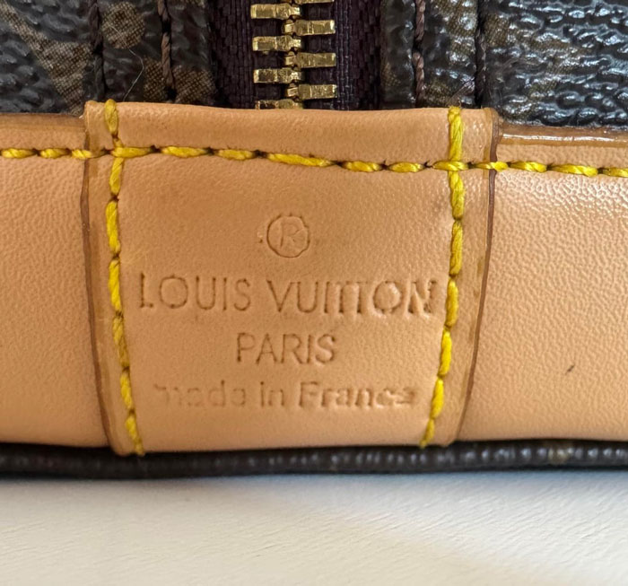 A close-up of a designer bag's label showing Louis Vuitton Paris, made in France, with visible stitching. This bag is a fake. A close-up of a designer bag's label showing Louis Vuitton Paris, made in France, with visible stitching. This bag is a fake.