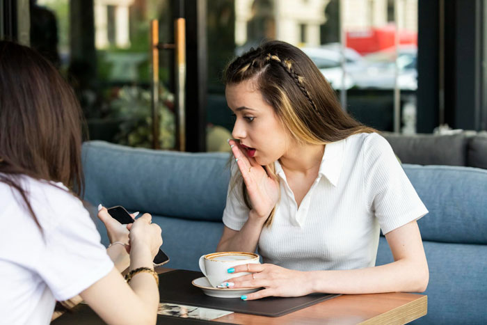 A woman looks shocked, holding her hand to her mouth, as her trusted friend discovers she received a fake designer bag. A woman looks shocked, holding her hand to her mouth, as her trusted friend discovers she received a fake designer bag.