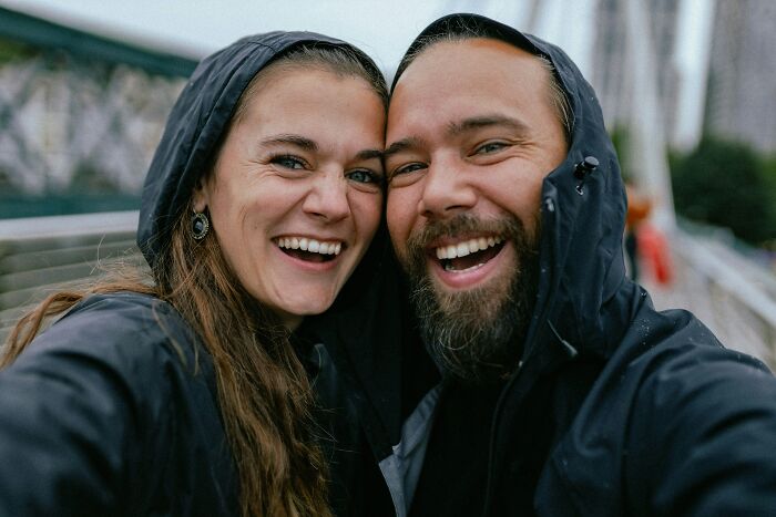 Joyful couple getting married, smiling brightly together in black hooded jackets.