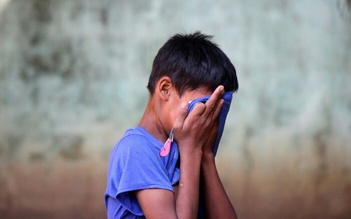 A young boy with dark hair covers his face with a blue cloth, possibly crying, illustrating extraordinary stories.
