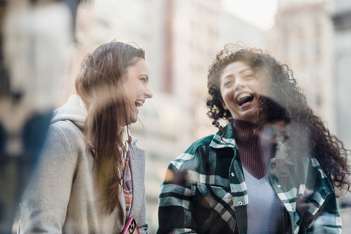 Two women laugh outdoors, reflecting the unexpected turn in a guy's relationship after a phone peek.