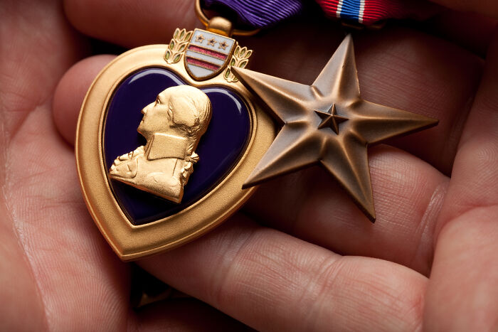 Hands gently hold a Purple Heart and a Bronze Star medal, symbolizing the extraordinary stories of bravery from World War II veterans.