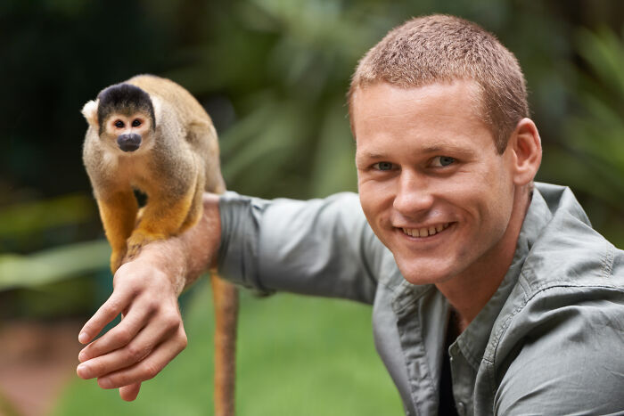 A smiling man with a squirrel monkey on his arm, showcasing interaction and guest house etiquette.