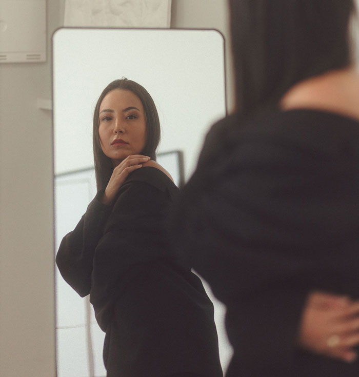 A woman looks at her reflection in a mirror, reflecting on her pursuit of the perfect body and the weight she lost.