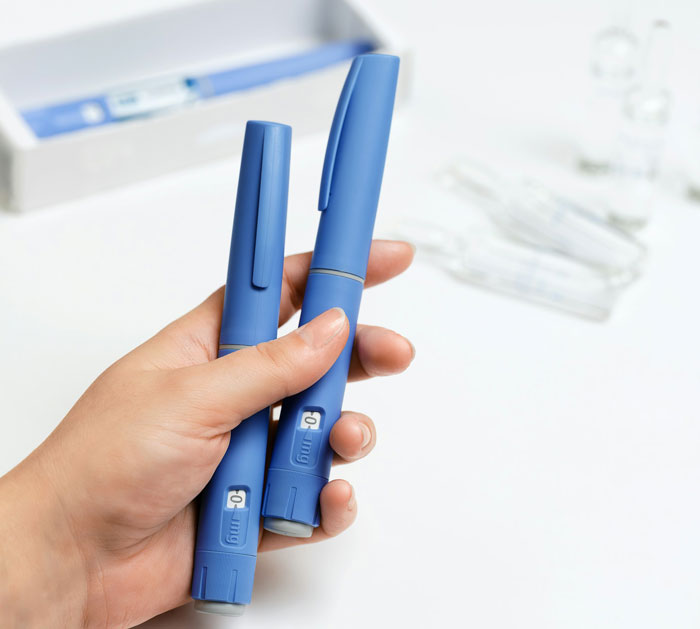 A hand holds two blue injection pens, symbolizing the use of medication in the pursuit of the perfect body and weight loss.