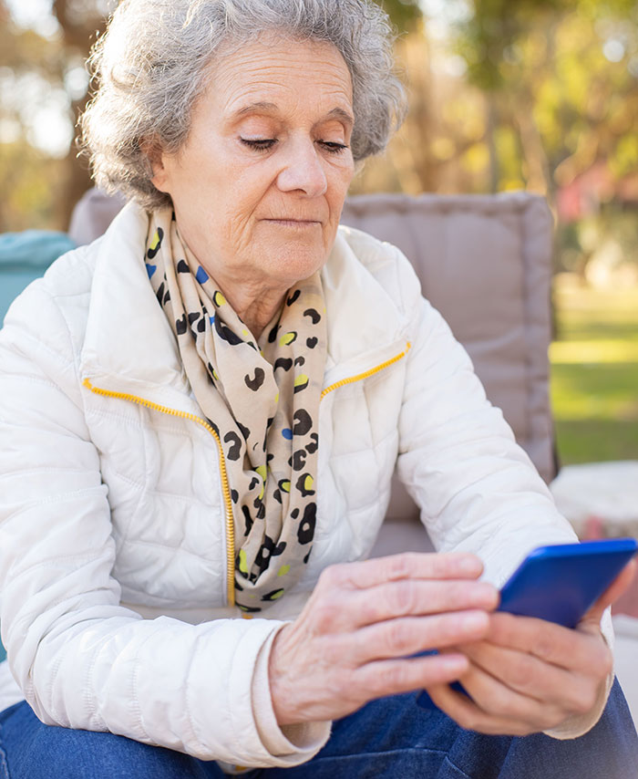 An older woman with grey hair looks at her phone, representing an entitled man's grandmother.