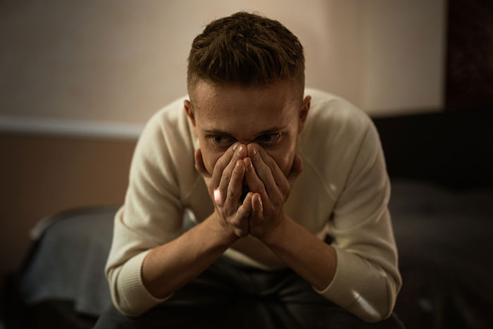 An entitled man, losing more than he bargained for, looks distraught with hands covering his face.
