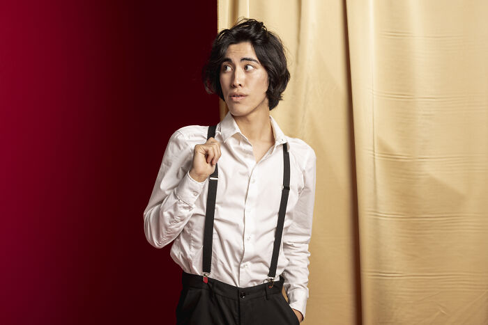 A young guy with a job making women swipe left poses in a white shirt with suspenders.