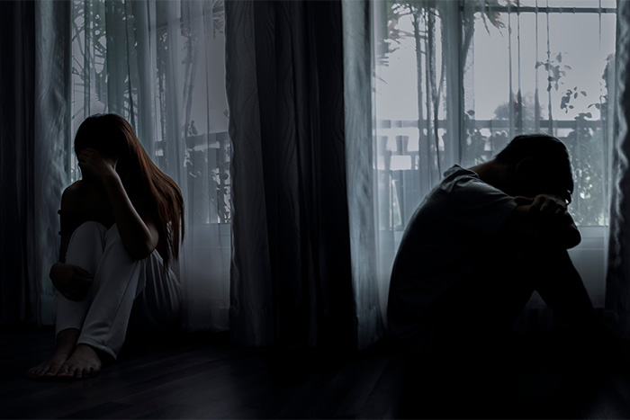 Two lonely figures, a man and a woman, sit apart in a dimly lit room, highlighting the harsh reality of loneliness. Two lonely figures, a man and a woman, sit apart in a dimly lit room, highlighting the harsh reality of loneliness.