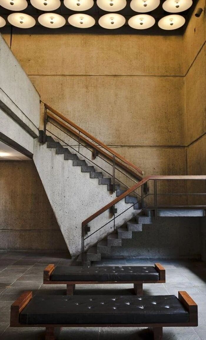 A modern concrete staircase with dark wood railings and black cushioned benches below, representing remarkable designs.