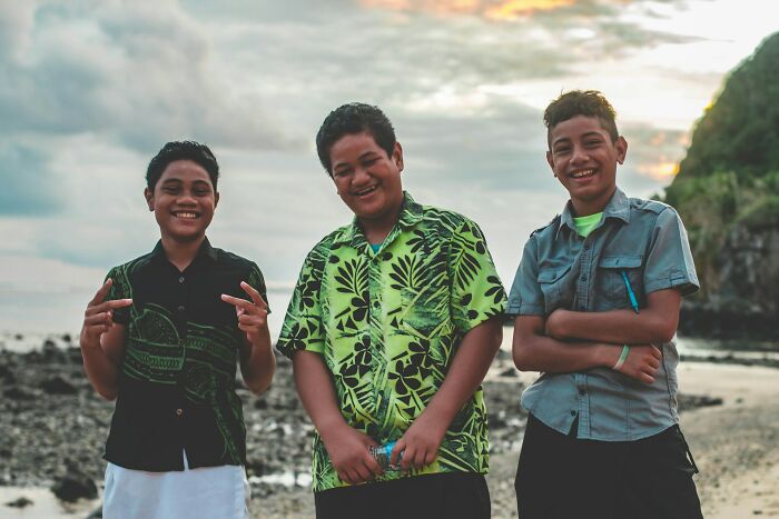 Three boys on a beach smiling at the camera, sharing their culture shocks with international partners.