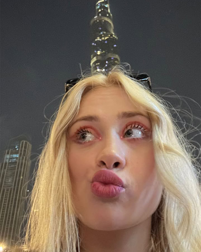 A close-up of a famous model with blonde hair making a funny face, with a tall building in the background at night. A close-up of a famous model with blonde hair making a funny face, with a tall building in the background at night.