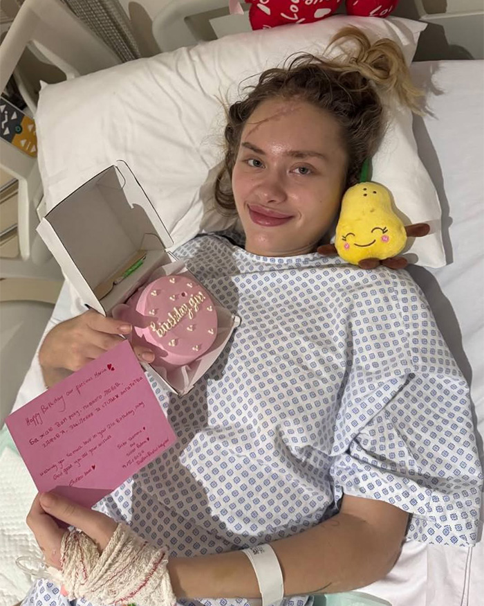A young woman recovering in a hospital bed with visible injuries, holding a small birthday cake. This model's fighting for life story highlights the challenges. A young woman recovering in a hospital bed with visible injuries, holding a small birthday cake. This model's fighting for life story highlights the challenges.