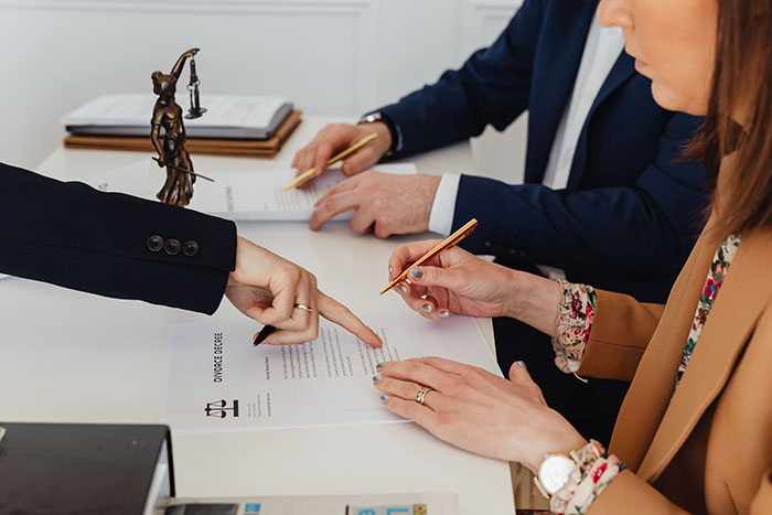 Two people are signing a divorce decree with lawyers. This shows the end of a marriage and wedding red flags.