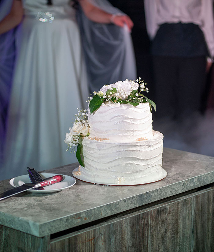 A beautiful two-tier wedding cake with white frosting and floral decorations, signifying the many wedding red flags.