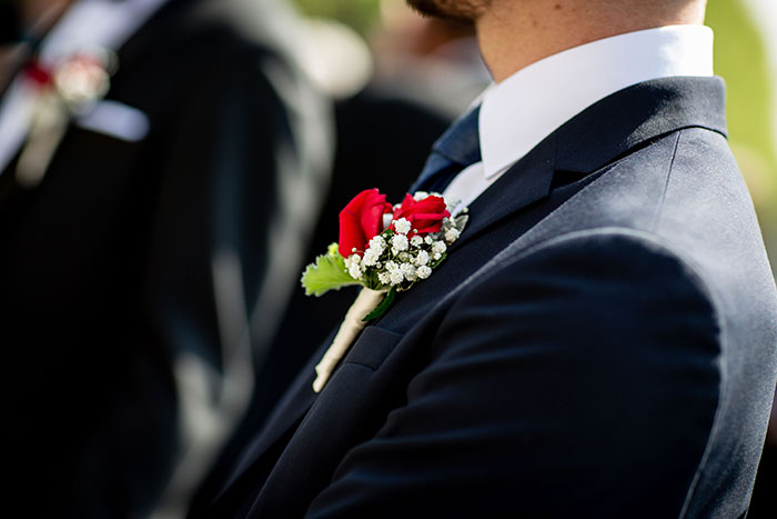 A close-up of a man's dark suit with a white shirt and a red rose boutonnière, symbolizing the formal attire at a wedding. This image represents the ceremonial aspects of a wedding, which can sometimes mask red flags.
