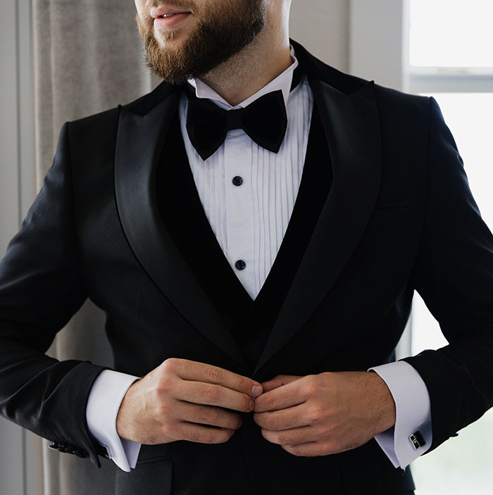 A groom in a tuxedo buttoning his jacket, displaying wedding attire that can have red flags.