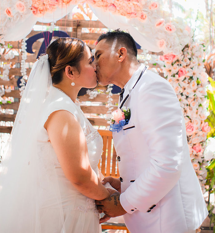 A bride and groom kiss under a floral arch, a snapshot of early wedding moments before any red flags.