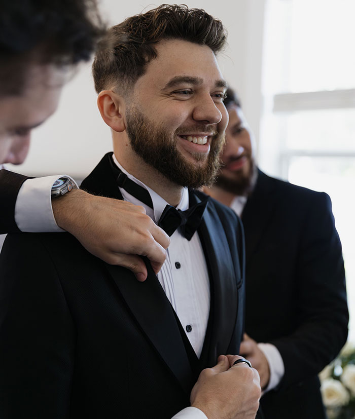 Groom smiling while getting ready for his wedding day with help from groomsmen, a potential wedding red flag.
