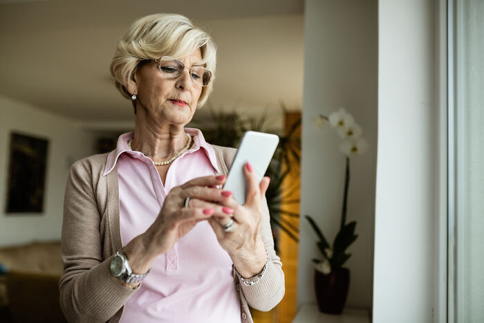 An older woman with glasses using a smartphone, perhaps sharing or reading stories about MILs.