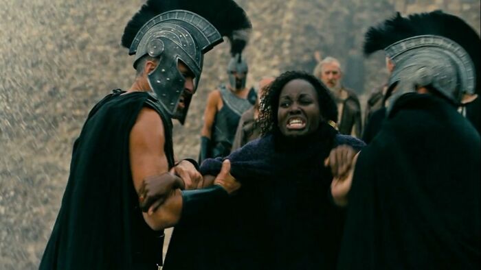 An actor in ancient armor restraining an emotional Black actress, relevant to The Odyssey casting backlash.