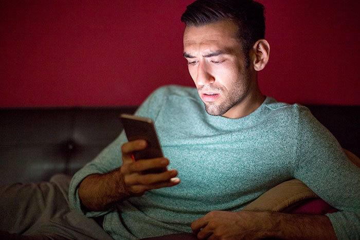 A man looking shocked while glancing at a phone in a dimly lit room, realizing his accidental peek changed everything.