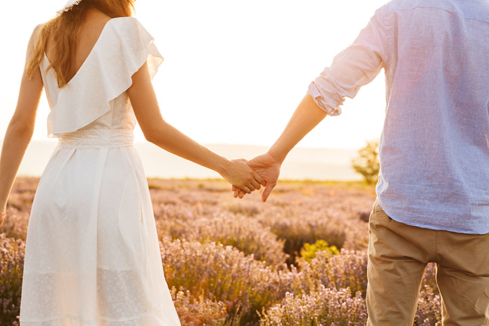 A couple holding hands, walking through a field of lavender at sunset, representing men dating women.