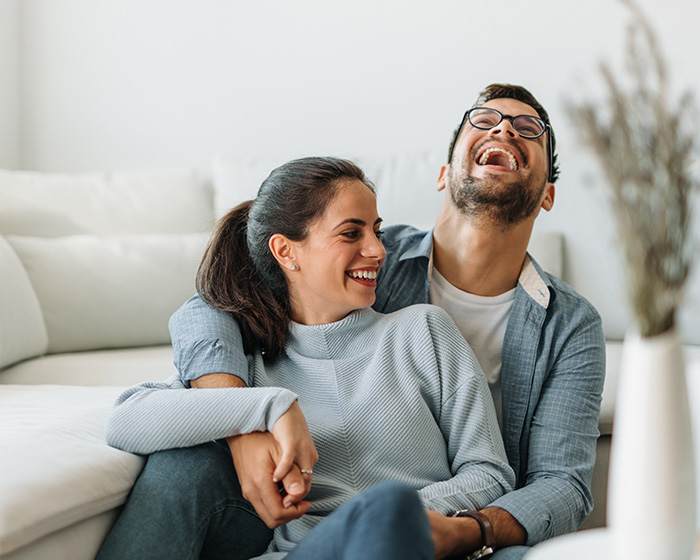 A happy couple sits on the floor, laughing together, embodying healthy relationships despite societal pressures on hips dips.