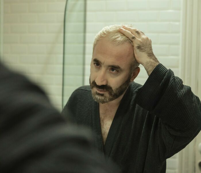 A man with a beard and bleached hair looks at his reflection in a mirror. Disturbing facts changed the way people see the world.