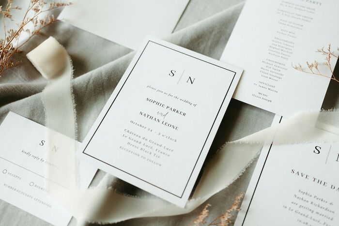 A close-up of wedding invitations laid out on a light grey fabric, with dried flowers and ribbon scattered around, highlighting micro feminism clap backs.
