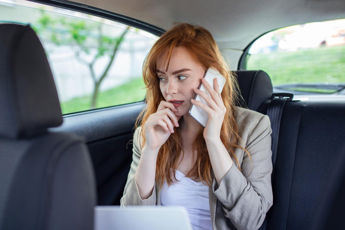 A woman with red hair in a car, looking worried while talking on a phone, representing the sister's unexpected reaction causing family drama. A woman with red hair in a car, looking worried while talking on a phone, representing the sister's unexpected reaction causing family drama.