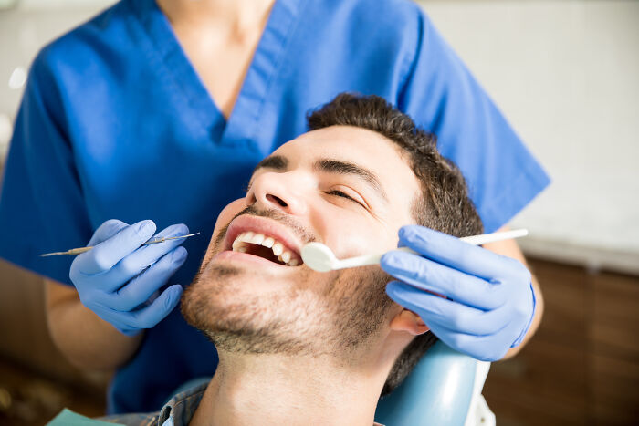 A man in a dental chair with a dentist examining his teeth, an example of a corporate practice in healthcare.
