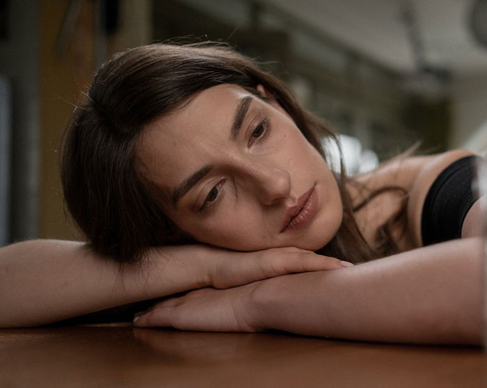 A woman rests her head on her arms looking down, feeling sad after her future mother-in-law called her defective.