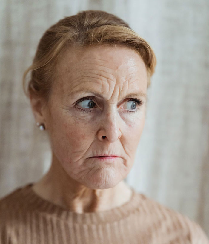 An older woman with a worried expression, representing the future mother-in-law calling the woman defective.