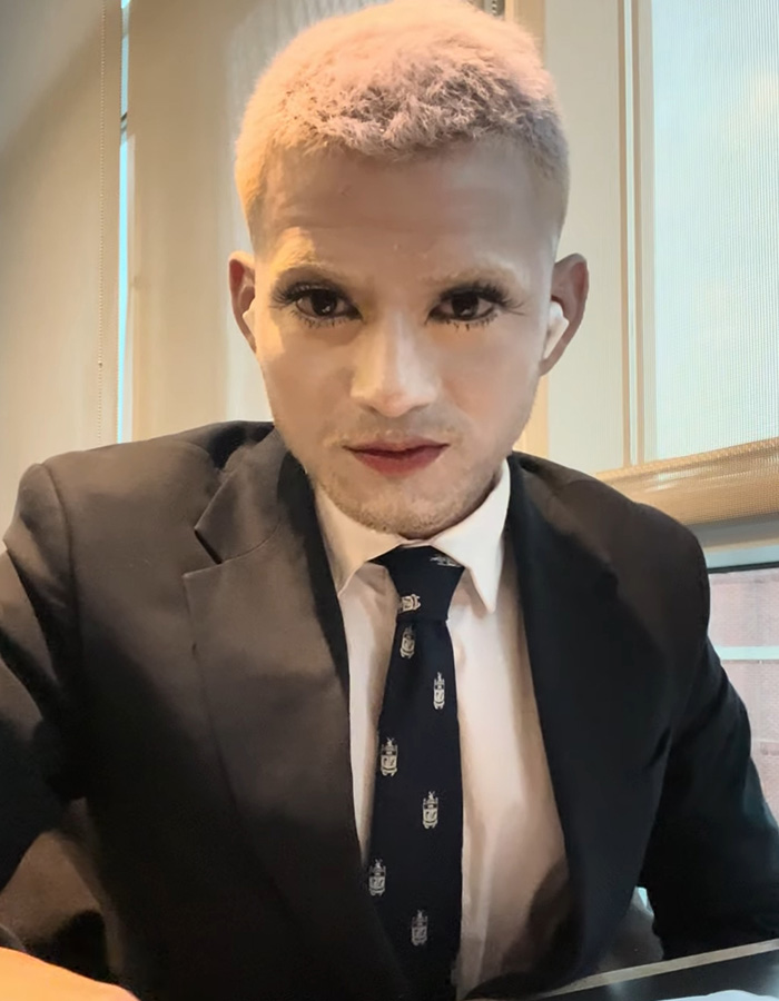 A mime with bleached hair and full make up, including dramatic eyelashes and lipstick, wearing a suit and tie. A mime with bleached hair and full make up, including dramatic eyelashes and lipstick, wearing a suit and tie.