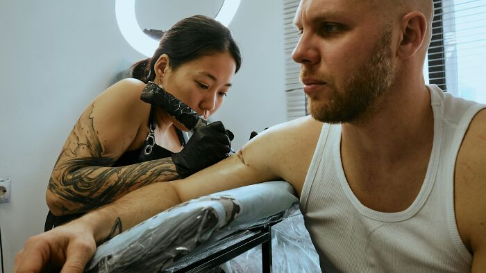 A female tattoo artist working on a client's arm, illustrating the dedication of tattoo artists to their craft.