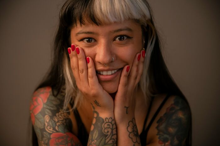 A woman with numerous tattoos on her arms and shoulders smiling, highlighting the work of tattoo artists.