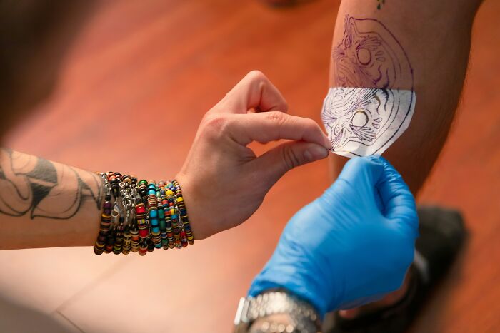 A tattoo artist applying a stencil to a client's leg, a crucial step before creating the permanent tattoo artwork.